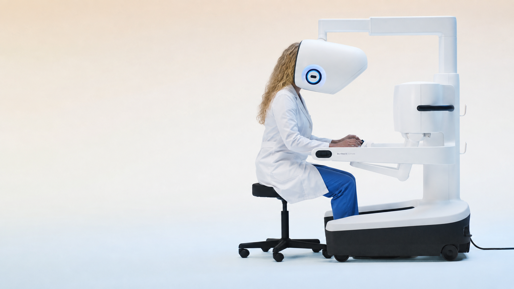 Dr. Wanda Good, DO, seen from the side in a white lab coat, leaning into the viewer of a robotic surgical console with one hand on the controls.